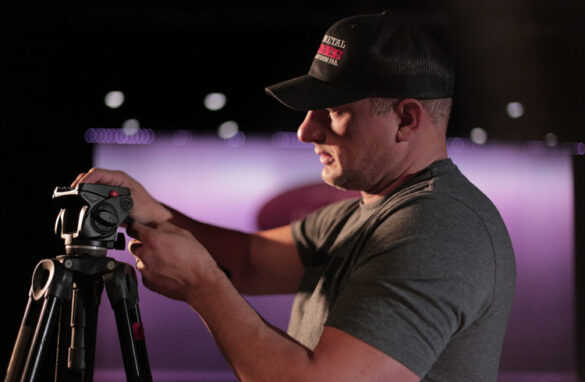 Keith Papke setting up a tripod in front of a stage lit by a purple light.
