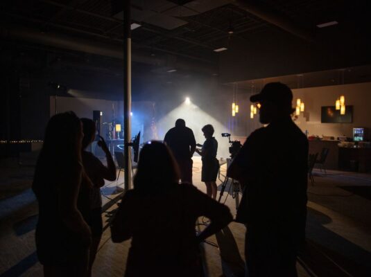 Video producers in vignette on a large set with one spotlight in the background.