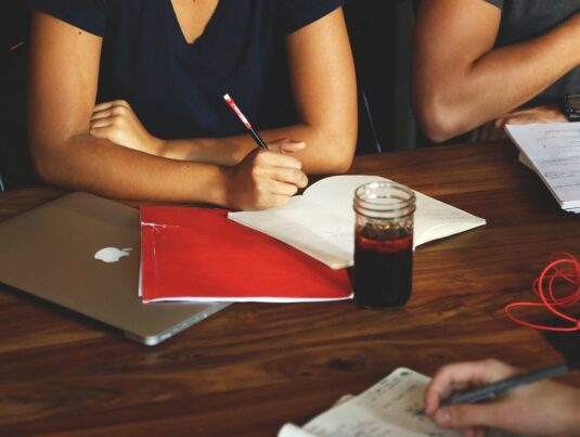 Woman with pencil and coffee taking notes in a meeting.